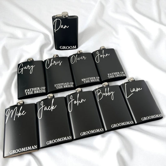 Black flasks with personalized names on a white fabric background